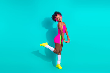 Smiling young woman in vibrant activewear posing confidently against a teal background showcasing stylish fitness fashion