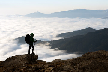 Fototapeta premium Silhouette of a hiker with a backpack against the background of foggy mountains. Travel and adventure concept