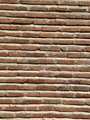 A rustic brick wall made of long, narrow, uneven red bricks laid in horizontal rows with light mortar between them. Close up