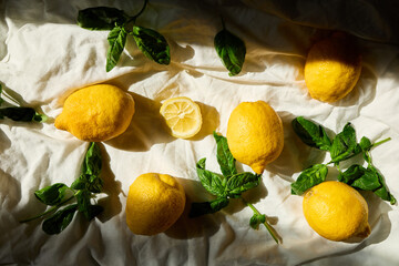 A collection of fresh lemons and vibrant basil leaves is artistically arranged on a light fabric...