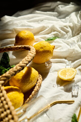 Lemons rest in a woven bag alongside fresh mint leaves and glassware, creating a vibrant summer feel on a sunlit cloth backdrop in Italy.