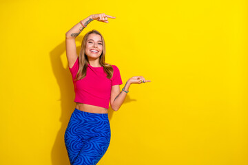 Cheerful young woman in stylish outfit gesturing happily against vibrant yellow background,...