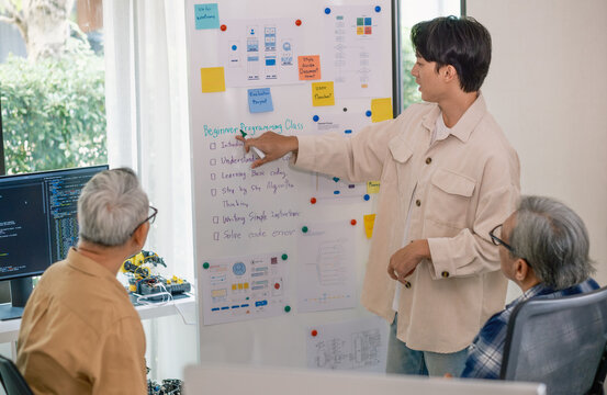 senior programmer bootcamlp,Asian young instructor guides senior learners through a programming on whiteboard, highlighting algorithm thinking and simple code exercises