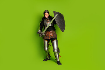Young man in medieval knight armor holding a sword and shield on a bright green background,...