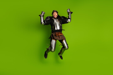 Young man in a medieval knight costume posing against bright green background, displaying...