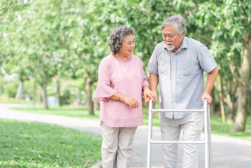 Happy in love Asian senior couple walking in the park. Senior man using walker