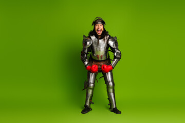 Knight in shining armor wearing red boxing gloves on green studio background