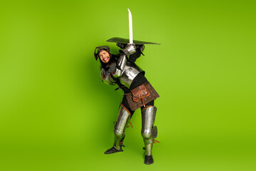 Young knight in medieval armor posing with a sword against a green background