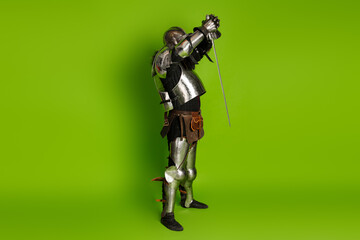 Medieval knight in full armor posing with a sword against a vibrant green background
