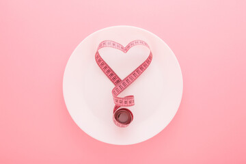 Heart shape created from measure tape on white plate on light pink table background. Pastel color....