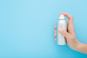 Young adult woman hand holding and showing gray metallic spray can on light blue wall background....