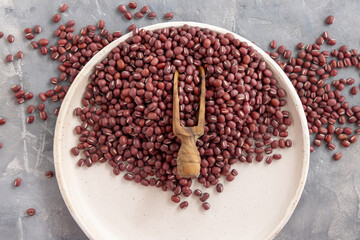 Plate full of dried red azuki beans with a wooden scoop top view. East Asian legumes, vegetarian food