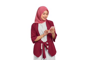Happy young Asian Muslim woman in hijab smiling and texting on smartphone isolated on transparent background