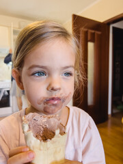 Little girl with a dirty face sits with chocolate ice cream in a waffle cup