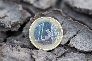 1 euro coin lying in cracked dry earth. A single euro coin resting in cracked, dry ground,...