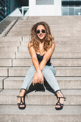 gl&uuml;ckliche junge Frau mit Sonnenbrille sitzt auf einer Treppe