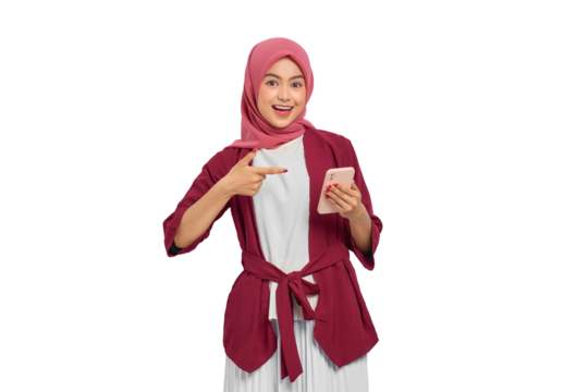 Excited young Asian Muslim woman in hijab pointing at smartphone with surprised expression isolated on transparent background - Powered by Adobe