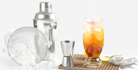 Glass of tasty Long Island iced tea, ice cubes and bartender tools on light background