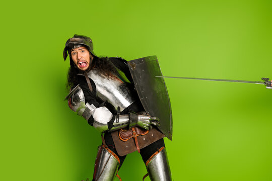 Young man in medieval knight armor with shield and sword on bright green background showcasing historical theme and humor