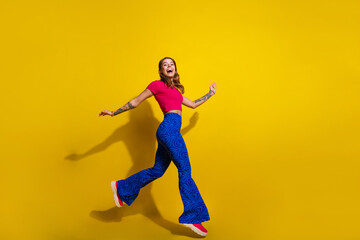 Fototapeta na wymiar Joyful young woman in stylish outfit happily jumping against bright yellow background