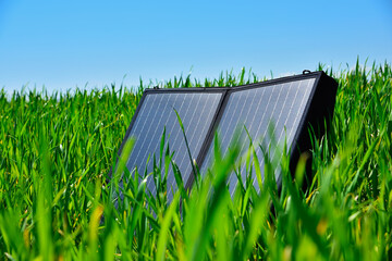 Portable solar panel standing in green grass under sunny blue sky outdoors.