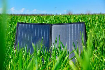 Portable solar panel standing in green grass under sunny blue sky outdoors.