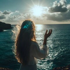 Woman with long hair is standing on a beach, holding her hand up in the air. The sun is shining brightly, creating a warm and inviting atmosphere. The ocean in the background is calm and peaceful