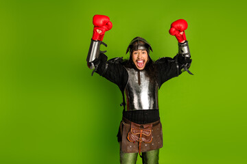 Young man dressed as a medieval knight celebrates victory with boxing gloves against a green...