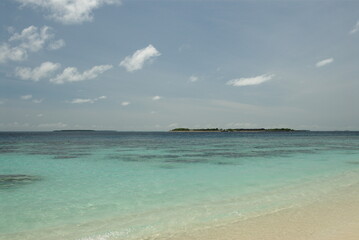 Pristine tropical beach with clear blue waters and distant islands under sunny sky