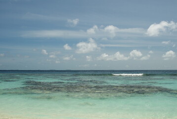 Tranquil azure ocean with white clouds and clear horizon under blue sky in the Maldives 