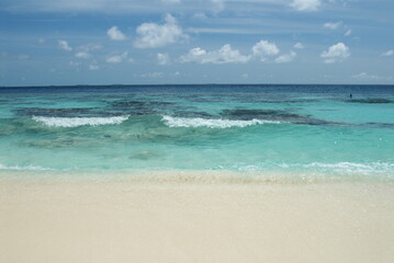 Serene tropical beach with turquoise waters and gentle waves under a clear sky in the Maldives 
