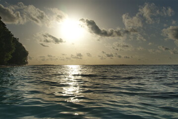 Obraz premium Serene ocean sunset with silhouetted trees and tranquil waves under cloudy sky in the Maldives 