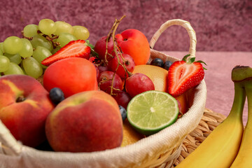 Wicker basket with different fresh fruits on pink table, closeup