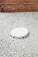 Minimalist white ceramic plate placed on a textured concrete surface with wooden backdrop. Ideal for food photography, tableware mockups, or clean modern kitchen-themed visuals.
