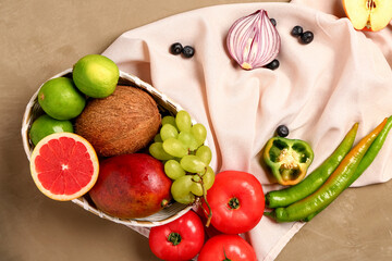 Wicker bowl with different fresh fruits and vegetables on brown background