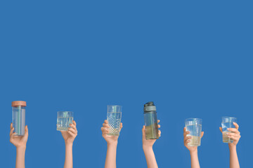Women holding sports bottles and glasses with clean water on blue background