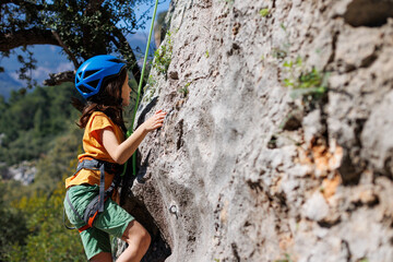boy climber in a helmet. A determined and strong boy climber climbs a steep mountain wall. A child...