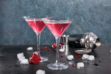 Glasses of Cosmopolitan cocktail with pomegranate and ice cubes on black table