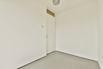 A simple, minimalist room showcasing plain white walls, a door, and a ceiling light, creating an...