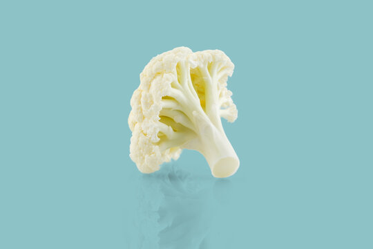 Fresh cauliflower floret resting on reflective surface with light blue background