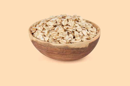 Rolled oats filling a rustic wooden bowl on a warm peach background