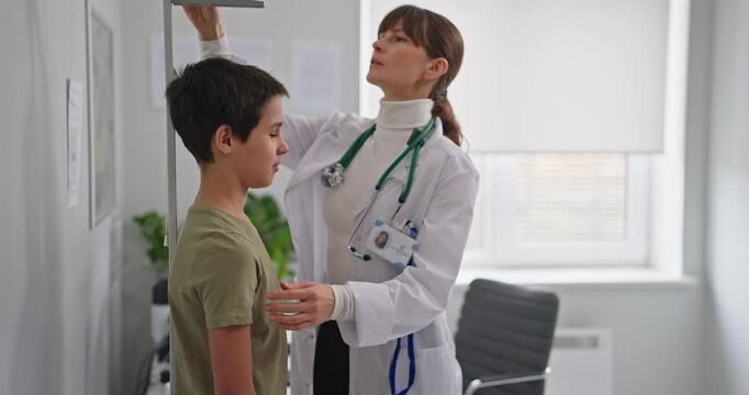 Female pediatrician doctor in white coat measures height of child boy during examination in modern hospital. Boy at a pediatrician appointment