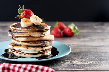 Pancakes with chocolate and fruit on wooden table. Copy space