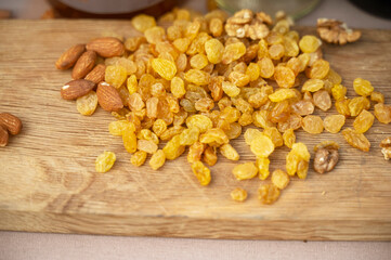 Light yellow raisins, almonds and walnuts lie on a natural wooden board