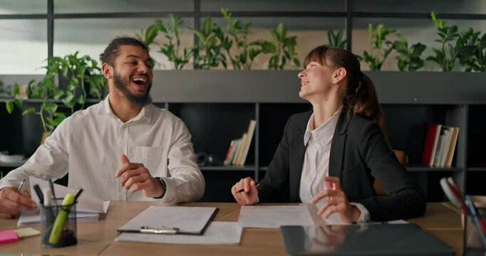 African office worker laughs and chats with a colleague at the table enjoying a casual conversation during a short work break