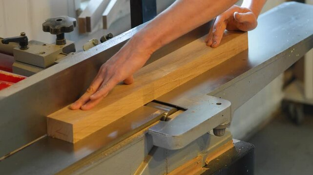 Carpenter hands smoothing wooden block on electric jointer machine. Man refining surface, eliminating imperfections, expert woodworking, finishing flawless carpentry detailing, meticulous adjustment