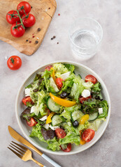 Fresh vegetable salad with feta cheese and olives on plate on a light background with glass of water.
