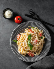 Creamy spaghetti with cherry tomatoes, parmesan cheese and basil on a plate on a dark background.