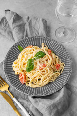 Creamy spaghetti with cherry tomatoes, parmesan cheese and basil on a plate on a light background
