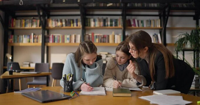In a charming library, enthusiastic schoolgirls actively engage in their studies while receiving guidance from their caring teacher in a collaborative setting